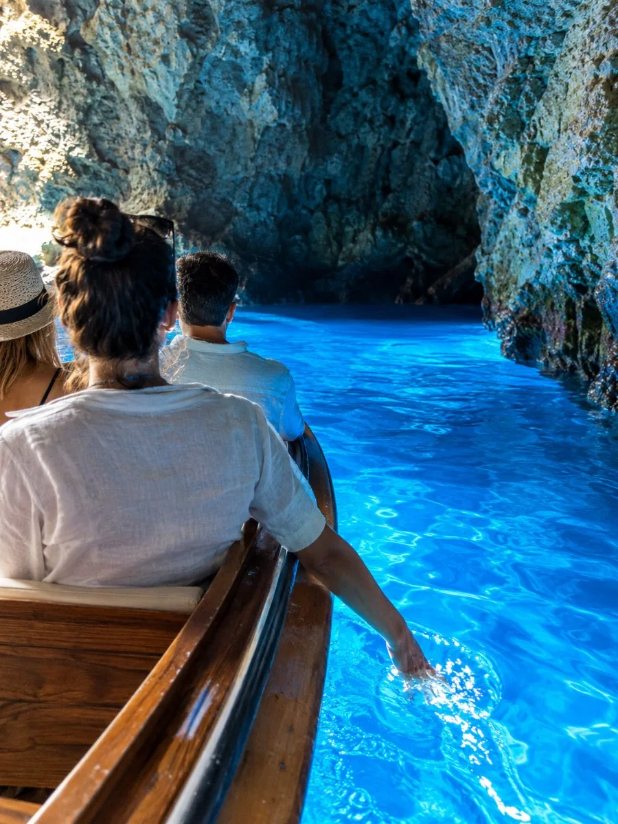 Visitors in a small wooden boat inside the Blue Cave, the water glowing blue beneath them